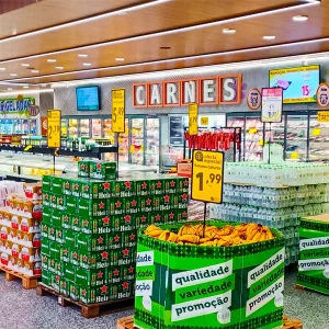 Supermercado com pedestal porta-cartaz posicionado ao lado de produtos em oferta, otimizando a comunicação no PDV com clareza e destaque.