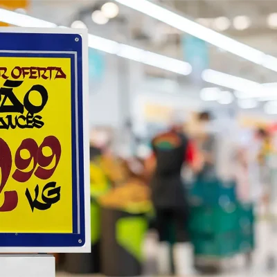Porta-cartaz com oferta de pão francês por R$ 9,99 o quilo em destaque no corredor de um supermercado.