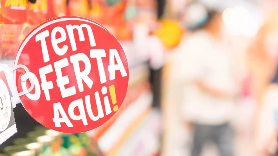 Sinalização vermelha com os dizeres “Tem Oferta Aqui!” destacando promoção em gôndola de supermercado, representando a exposição estratégica de ofertas.