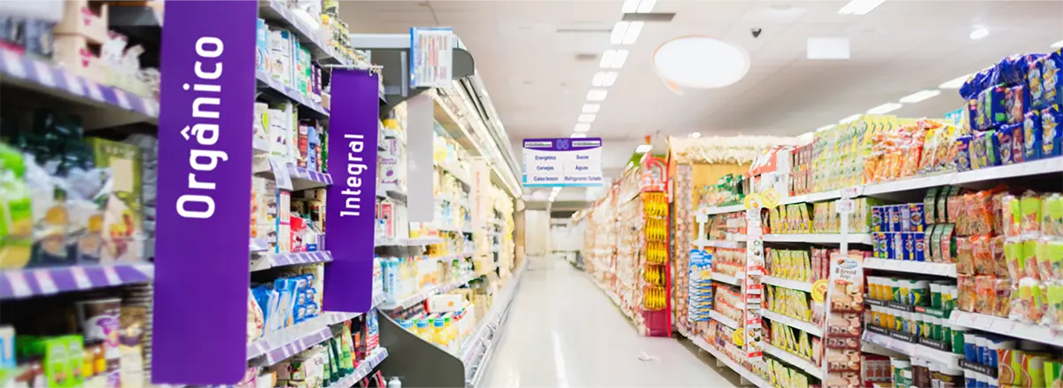 Corredor de supermercado com placas verticais “Orgânico” e “Integral” como exemplo de comunicação visual para aumentar ticket médio no supermercado.