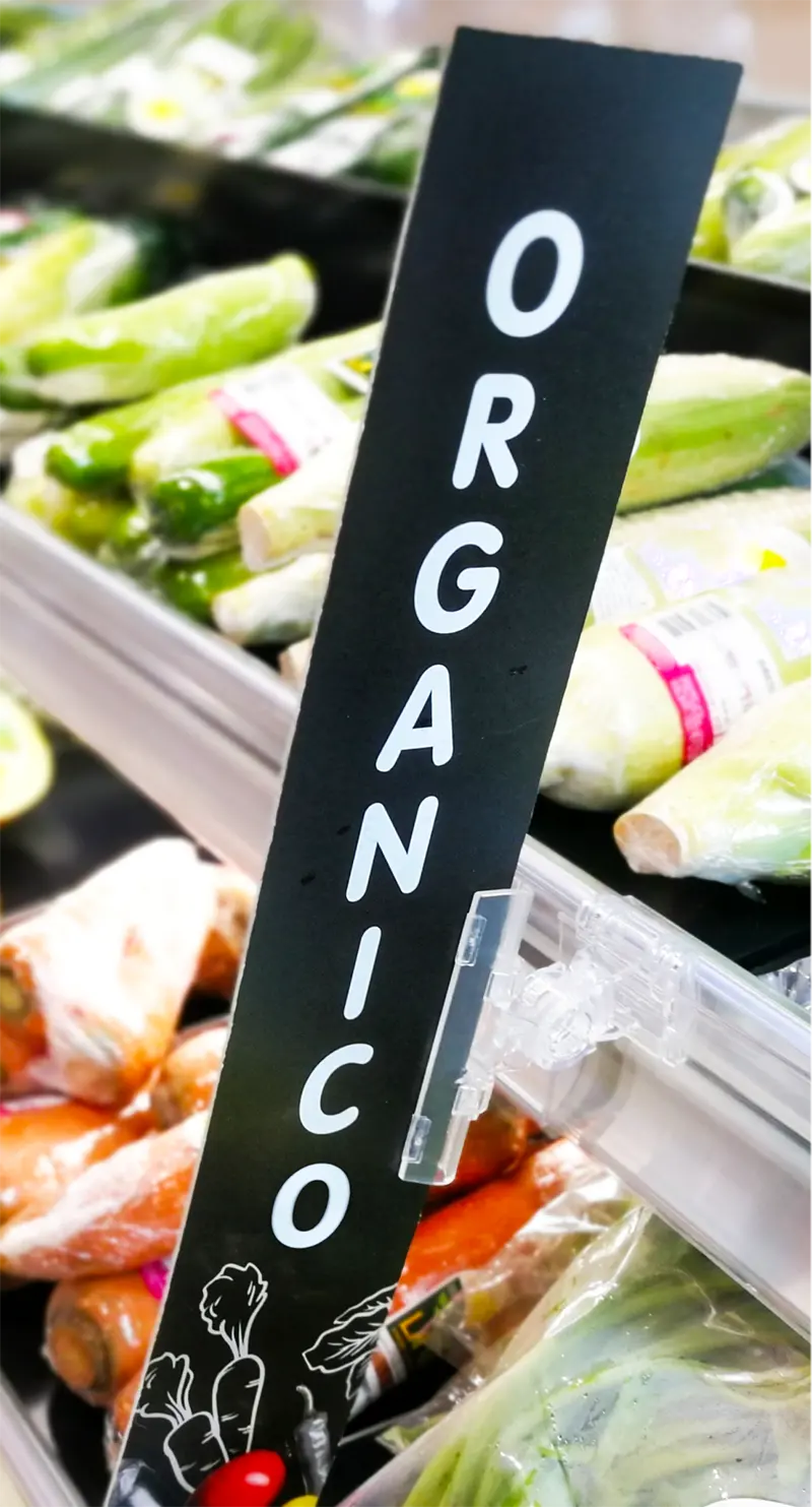 Placa vertical com a palavra “Orgânico” em gôndola de hortifrúti, ilustrando comunicação visual para aumentar ticket médio no supermercado.