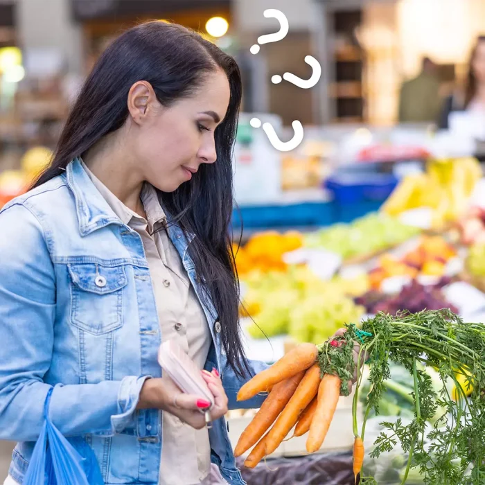 Mulher segurando um maço de cenouras em um mercado, refletindo como a transparência nos preços influencia a decisão de compra.