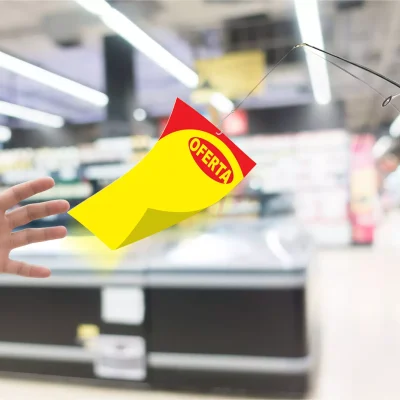Mão tentando alcançar um cartaz amarelo e vermelho com a palavra “OFERTA” pendurado em uma vara de pescar, representando a dificuldade de manter as vendas após a Black Friday.