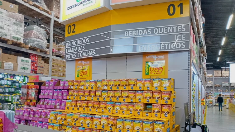 Área de atacarejo com cartazes promocionais e sinalização de corredores, mostrando como Organizar a Comunicação de Preços para Vender Mais com destaque visual e organização de gôndolas.