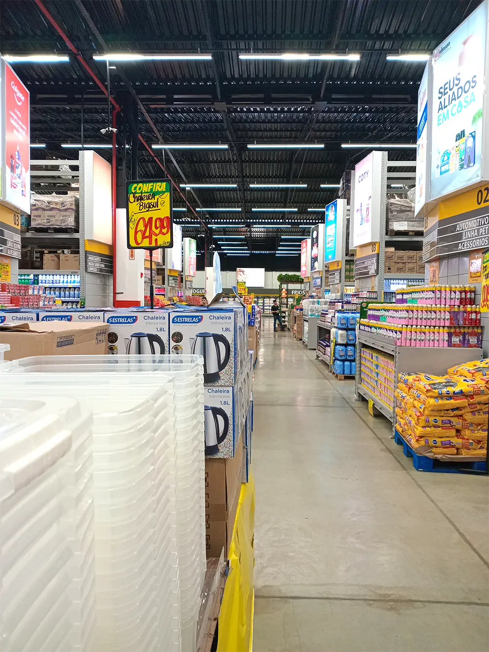 Como Organizar a Comunicação de Preços para Vender Mais com destaque e clareza no PDV Vista de um corredor de atacarejo com cartazes promocionais e prateleiras organizadas, mostrando boas práticas para Organizar a Comunicação de Preços para Vender Mais e atrair o consumidor.