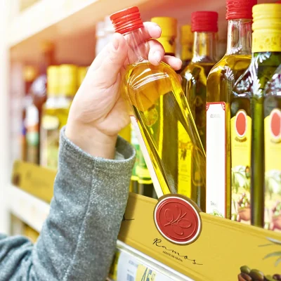Consumidor escolhendo azeite em gôndola de supermercado com comunicação visual destacada, exemplo de Retail Media aplicado no ponto de venda.