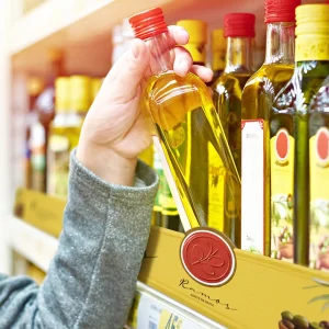 Consumidor escolhendo azeite em gôndola de supermercado com comunicação visual destacada, exemplo de Retail Media aplicado no ponto de venda.