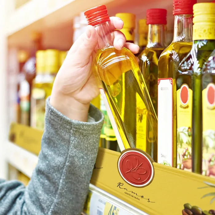 Consumidor escolhendo azeite em gôndola de supermercado com comunicação visual destacada, exemplo de Retail Media aplicado no ponto de venda.