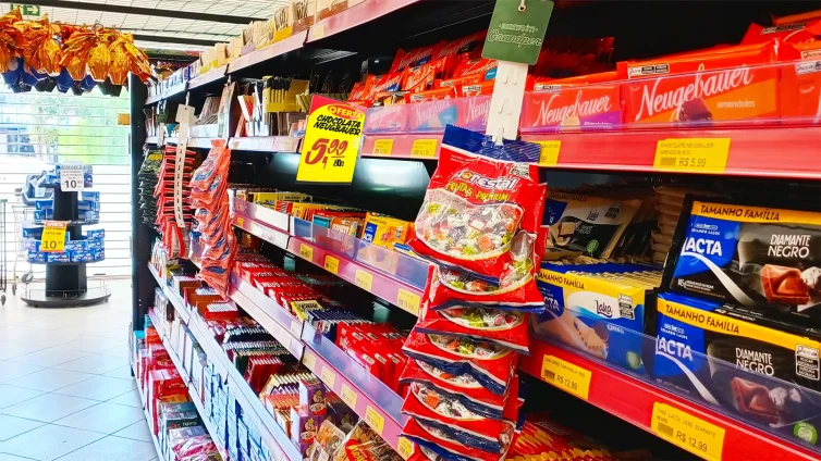 Sua gôndola comunica ou confunde. Gôndola de supermercado com chocolates organizados, etiquetas de preço e cartazes promocionais destacando ofertas, mostrando como a comunicação visual influencia a decisão de compra.