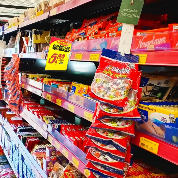 Gôndola de supermercado com chocolates organizados, etiquetas de preço e cartazes promocionais destacando ofertas, mostrando como a comunicação visual influencia a decisão de compra.